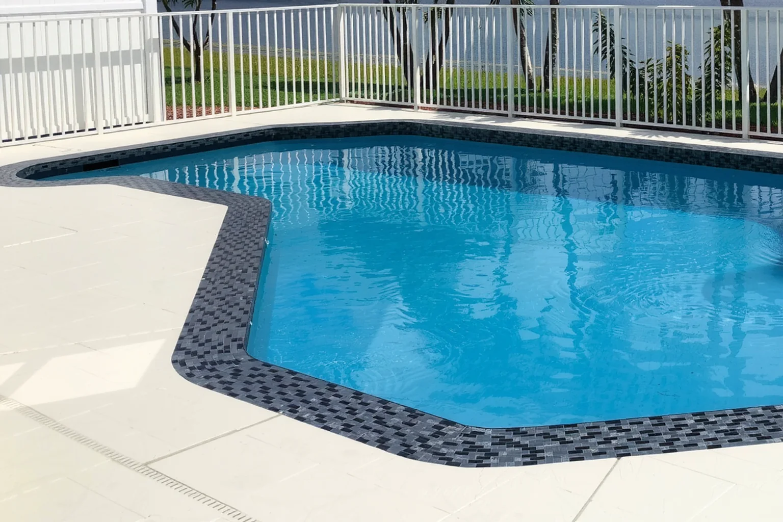 Continuous mosaic coping around an inground pool beside a level pale deck