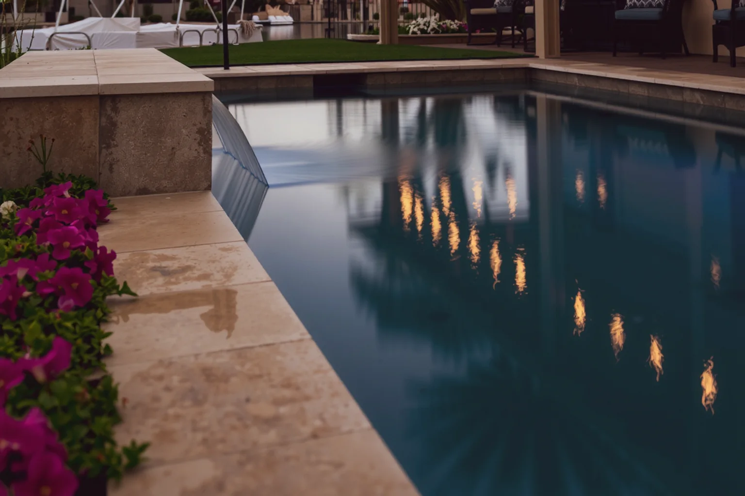 Dusk reflections in an inground pool beside a stone spa spillway and covered patio