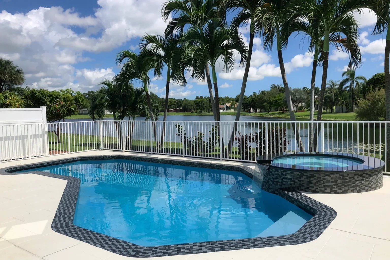 Inground backyard pool and round spillover spa with mosaic coping and a pale deck