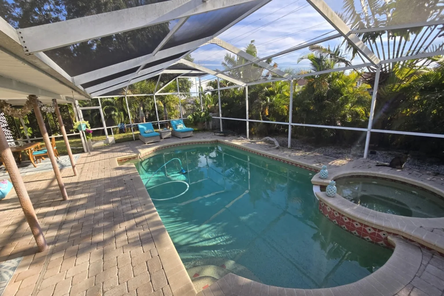 Screened backyard pool and round spa with paver decking and tropical planting